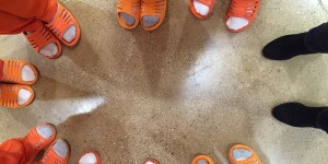 feet of people standing in a circle. Feet are in socks and orange sandals.
